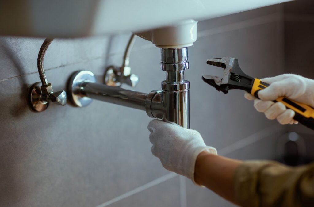 Experienced plumber diagnosing burst pipe emergency with tools near shutoff valve. Plumber Near Me.