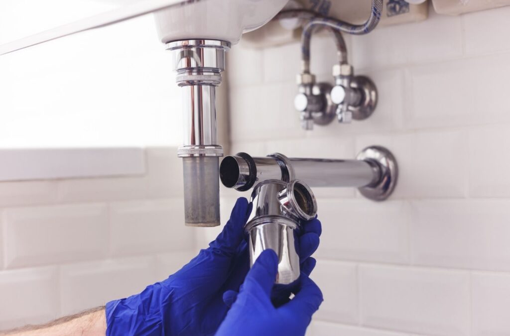 Plumber stopping active water leak under sink during urgent residential service call