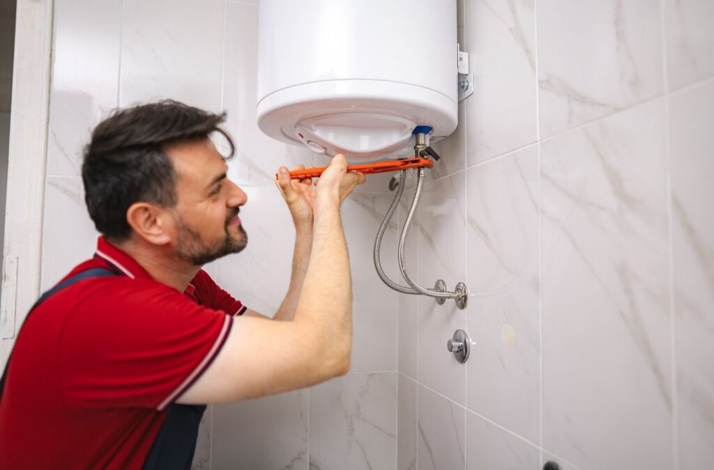Plumber diagnosing failed water heater controls with testing tools in tight utility room